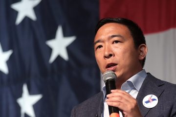 Andrew Yang speaking in front of flag